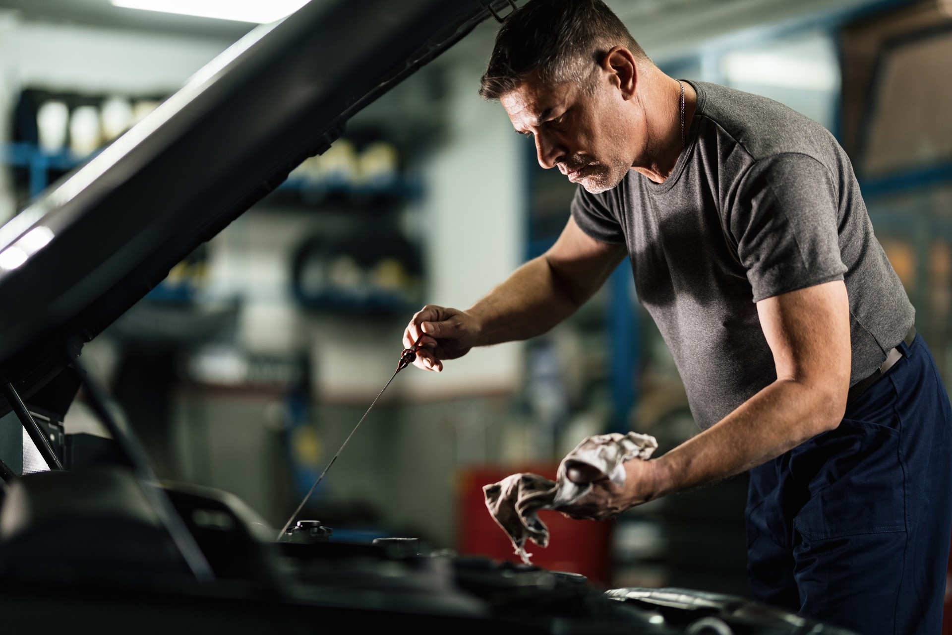 Auto mechanic checking car oil in a repair workshop.