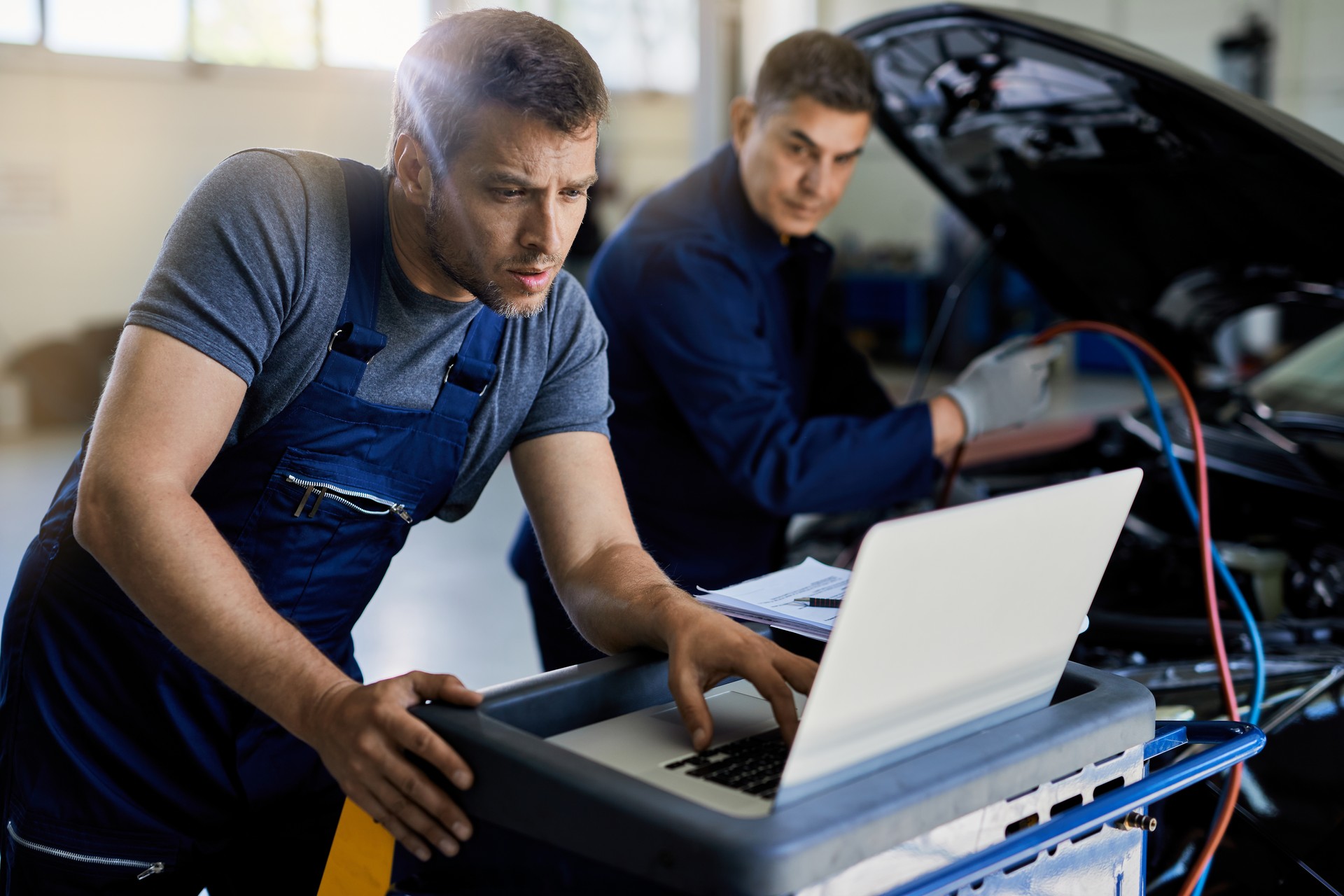 Mid adult mechanic using laptop while running car diagnostic in auto repair shop.