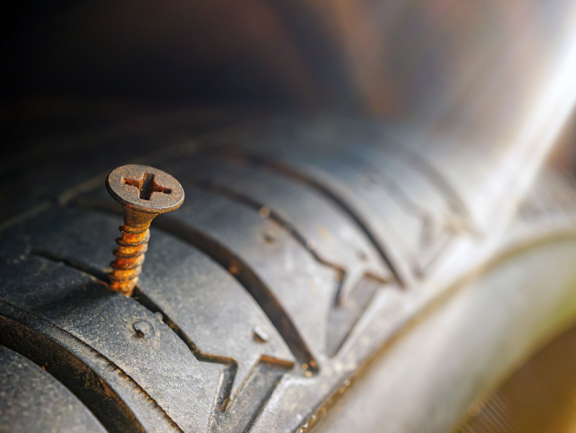 Close-up of a rusty screw driving into a car tire causing a puncture.
